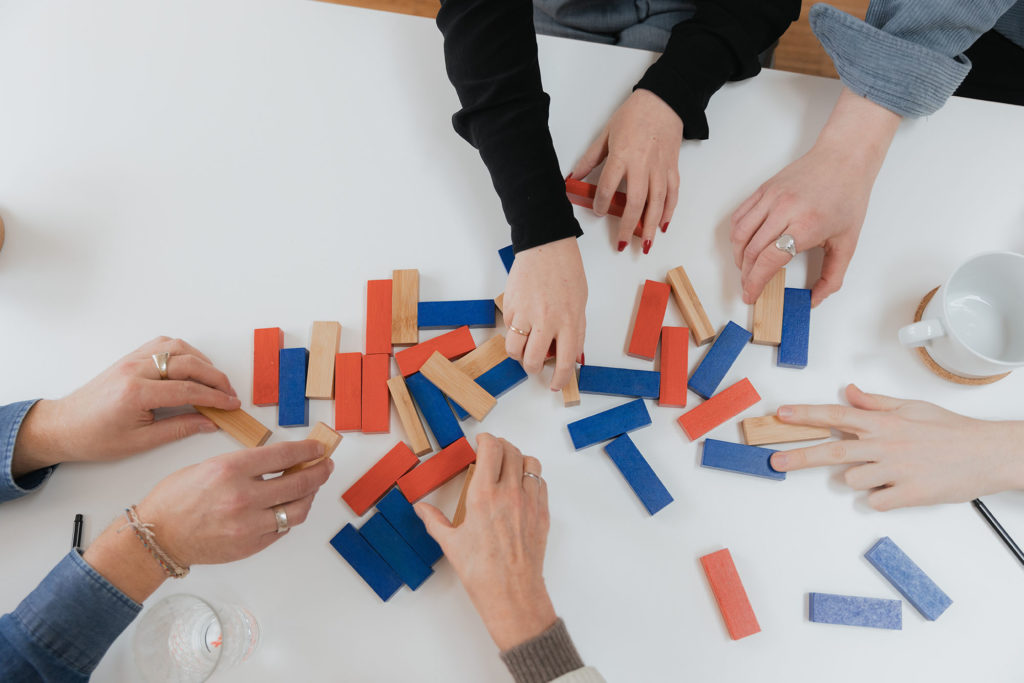 Hände arbeiten zusammen an einer Problemlösung, symbolisch mit Jenga Steinen